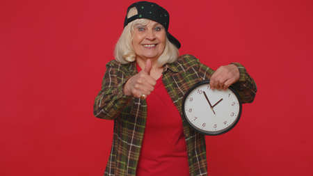 It is your time. Portrait of senior woman in shirt showing time on clock watch, ok, thumb up,...