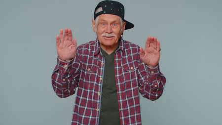 Handsome senior man in shirt smiling friendly at camera and waving hands gesturing hello or goodbye,...