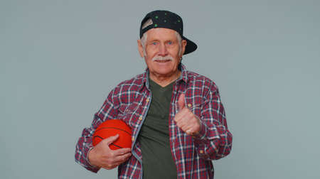 Senior man sportsman basketball fan holding ball looking at camera, training dribbling. Workout...