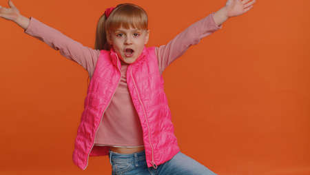 Funny happy sincere little girl 6 years old in vest making playful silly facial expressions and...