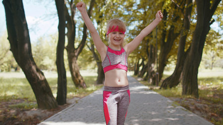 Athletic fitness sport runner child girl finishing racing competition. Victory and success. Workout cardio training in park. Toddler kid jogger champion winning marathon. Active children motivationの写真素材