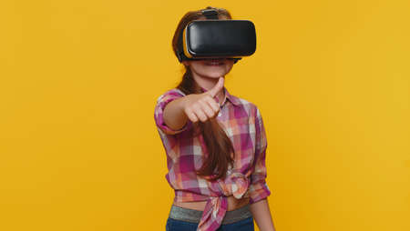 Young preteen child girl kid using virtual reality futuristic technology VR app headset helmet to play simulation 3D 360 video game, watching film movie. Little toddler children on yellow backgroundの写真素材
