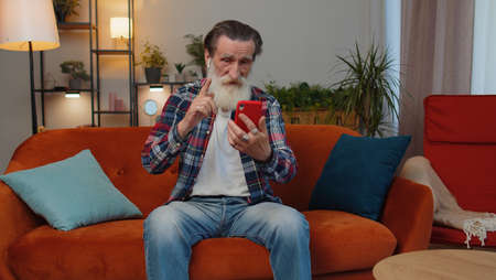 Senior old grandfather man wearing earphones making phone online conversation call with family...