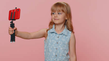 Young preteen child girl kid blogger taking selfie on smartphone selfie stick, communicating video...