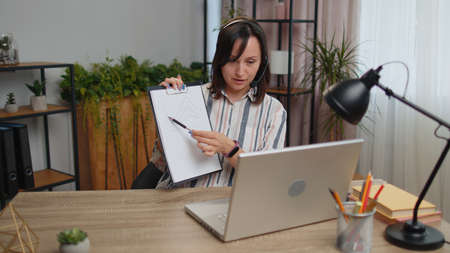 Young business woman sitting at desk at home office wearing headset, freelance worker, call center,...