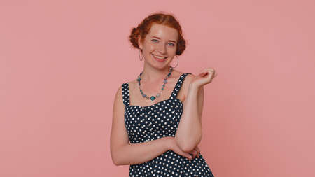 Cheerful lovely redhead young woman in black dress smiling, looking at camera, flirting. Adult fashion red hair model girl indoors studio shot isolated on pink background. Female nature beautyの写真素材