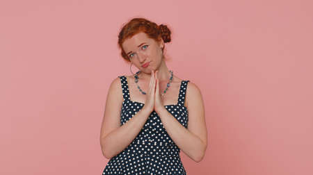 Please, God help. Young redhead woman praying, looking upward and making wish, asking with hopeful imploring expression, begging apology. Ginger girl with freckles isolated on pink studio backgroundの写真素材
