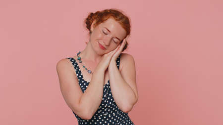Tired young redhead woman in dress yawning, sleepy inattentive feeling somnolent lazy bored gaping suffering from lack of sleep. Ginger girl with freckles isolated alone on pink studio backgroundの写真素材