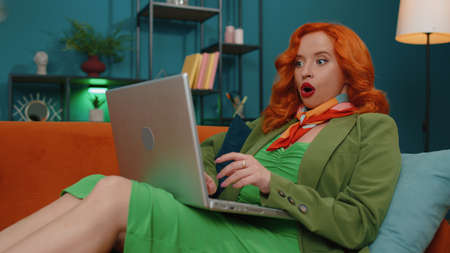 Oh my God Wow. Amazed redhead young woman use laptop computer, receive good news message, shocked by...