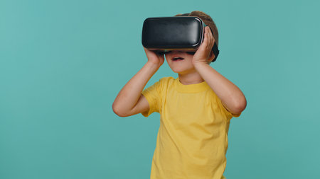 Little toddler children boy using headset helmet app to play simulation game. Watching virtual reality 3D 360 video film. Young preschool kid in VR goggles isolated alone on blue studio backgroundの写真素材