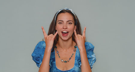Overjoyed delighted pretty woman showing rock n roll gesture by hands, cool sign, shouting yeah with...