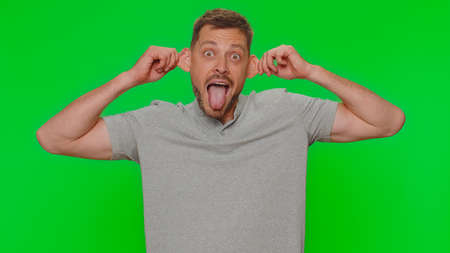 Bearded handsome funny man in t-shirt making playful silly facial expressions and grimacing, fooling around, showing tongue. Adult male guy isolated alone on chroma key studio background indoorsの写真素材