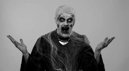 Oh my God, Wow. Frightening man with Halloween zombie bloody wounded makeup raising hands in surprise looking at camera with big eyes, shocked by sudden victory. Excited amazed sinister undead guyの写真素材