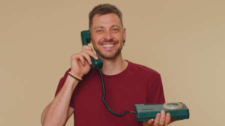 Hey you, call me back. Handsome young man in red t-shirt talking on wired vintage telephone of 80s,...