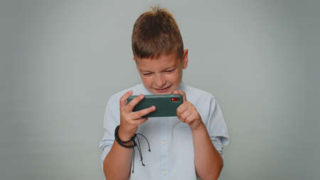 Worried funny addicted children boy enthusiastically playing racing video games on mobile phone....