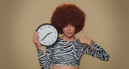 It is your time. Pretty young woman with brown lush wig showing time on wall office clock, ok, thumb...