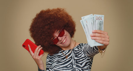 Happy young woman with lush wig looking smartphone display sincerely rejoicing win, receiving money...