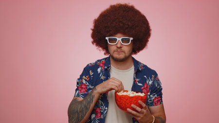 Excited tourist man in 3D glasses enjoying eating popcorn and watching interesting tv serial sport...