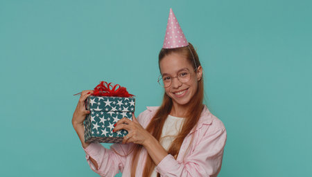 Cheerful lovely pretty teenager girl receiving gift box and smiling joyfully, looking amazed satisfied with nice present, unexpected birthday surprise. Teen female child kid on blue studio backgroundの写真素材