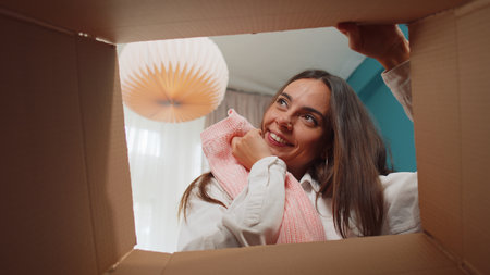 Portrait of happy girl unpacking delivery parcel sitting at home. Smiling satisfied young woman shopper, online shop customer opening cardboard box receiving purchase gift by fast postal shippingの写真素材