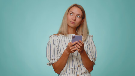 Blonde young woman in crop top using smartphone typing new post on web, sms message, browsing,...