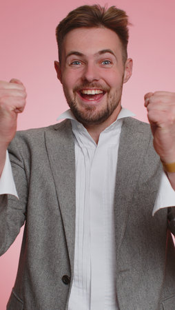 Happy joyful business office man shouting, raising fists in gesture I did it, celebrating success, winning, birthday, lottery goal achievemen. Adult guy boy indoors on pink studio background. Verticalの写真素材