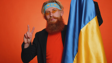 Redhead bearded man holding Ukraine national flag, showing victory sign against war, hoping for success and win, doing peace gesture, smiling with kind optimistic expression. Young ginger guy boyの写真素材