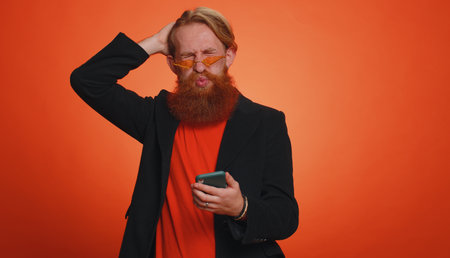 Bearded man in jacket use mobile cell phone typing browsing, loses becoming surprised sudden lottery...