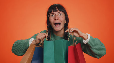 Happy tourist woman in green sweater showing shopping bags, advertising discounts, smiling looking...