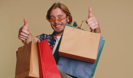 Happy tourist man in checkered shirt showing shopping bags, advertising discounts, smiling looking...