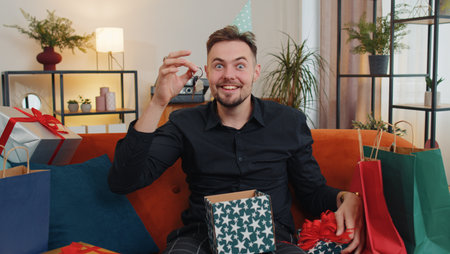 Happy young bearded man wears festive birthday cap hat hold gift box with ribbon congratulating....