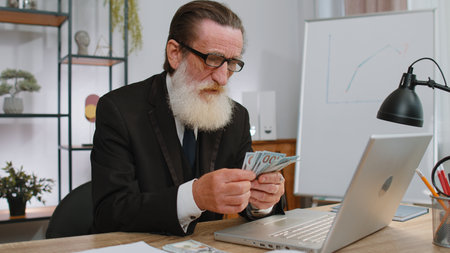 Rich senior businessman working on laptop pc counting money cash, calculate earnings income profit at office workplace. Professional manager freelancer man. Business old people. Employment, occupationの写真素材