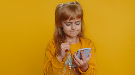 Young toddler school girl in sweater use smartphone typing browsing, loses becoming surprised sudden...