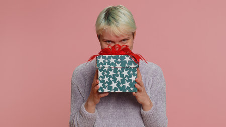 Positive smiling woman presenting birthday gift box stretches out hands, offer wrapped present...