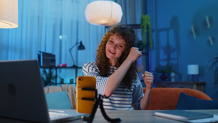 Young woman sitting at the desk blogger taking selfie on smartphone tripod communicating video call...