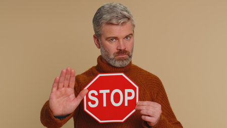 Serious middle-aged man say No, hold inscription text red No stop danger sign, warning of finish,...
