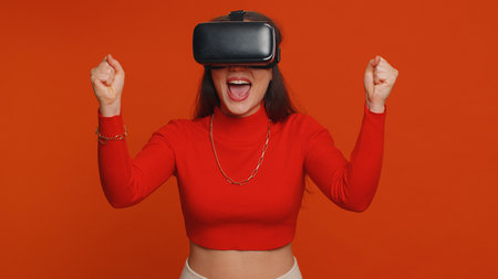 Lovely woman using headset helmet to play simulation game app online. Watching virtual reality 3D 360 video content. One girl in VR goggles isolated on studio red background. Futuristic technologyの写真素材