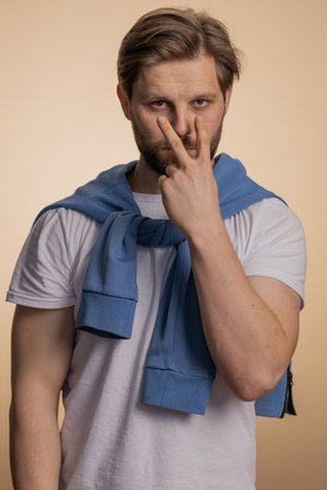 I am watching you. Young confident caucasian man pointing at his eyes and camera, show I am watching you gesture, spying on someone. Handsome bearded guy isolated alone on beige studio backgroundの写真素材