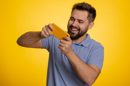 Worried funny addicted caucasian man enthusiastically playing racing video games on mobile phone....