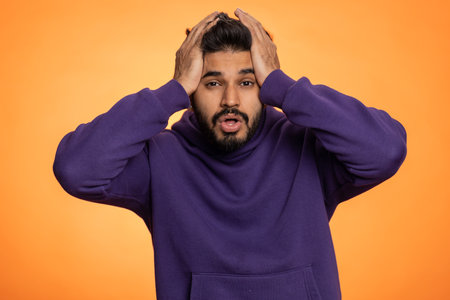 Bearded indian man feeling hopelessness loneliness, nervous breakdown, loses becoming surprised by lottery results, bad fortune loss, unlucky news. Hindu young guy isolated on studio orange backgroundの写真素材