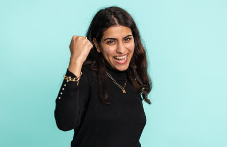 Happy joyful indian woman shouting, celebrating success, winning, birthday, lottery jackpot goal achievemen, good news, victory. Young hindu girl isolated on blue studio backgroundの写真素材