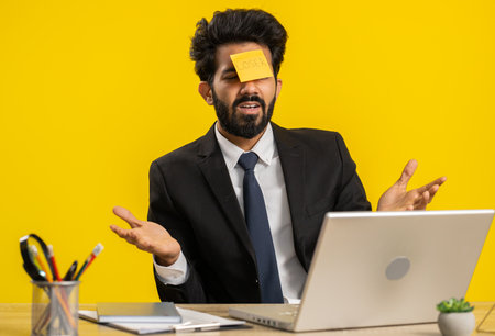 Indian businessman with loser sticker on forehead working on laptop loses becoming surprised by bad...