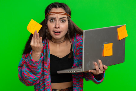 Exhausted freelancer woman with pasted sticker notes use laptop computer having concentration problem creative crisis. Nervous girl confused by big routine work loading on green chroma key backgroundの写真素材