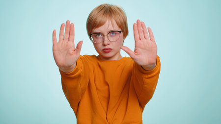 Young woman say No hold palm folded crossed hands in stop gesture, warning of finish, prohibited access, declining communication, body language, danger. Girl on blue background. People lifestylesの写真素材