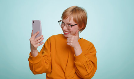 Woman blogger in glasses, taking selfie vlog on smartphone, communicating video call online with...