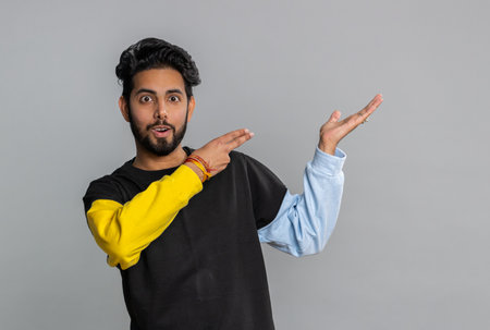 Young indian man showing thumbs up and pointing empty place, advertising area for commercial text,...