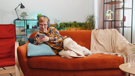 Portrait of happy overjoyed woman in wireless headphones relaxing lying on couch at home apartment choosing listening favorite energetic disco dancing music. People weekend daytime leisure activitiesの写真素材
