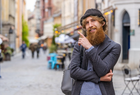 Thoughtful pensive puzzled man with pensive expression, pondering a solution, doubting question, thinking inspiration dreaming outdoors. Bearded guy in city street pointing empty place. Copy-spaceの写真素材