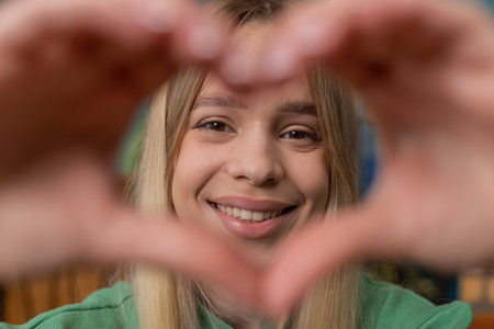 I love you. Happy Caucasian woman at home living room couch makes symbol of love, showing heart sign to camera, express romantic feelings express sincere positive feelings. Charity, gratitude donationの写真素材