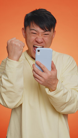 Happy excited joyful asian man use smartphone typing browsing shouting say wow yes found out great big win, good news, lottery goal achievemen, celebrating success, winning game. Vertical shotの写真素材